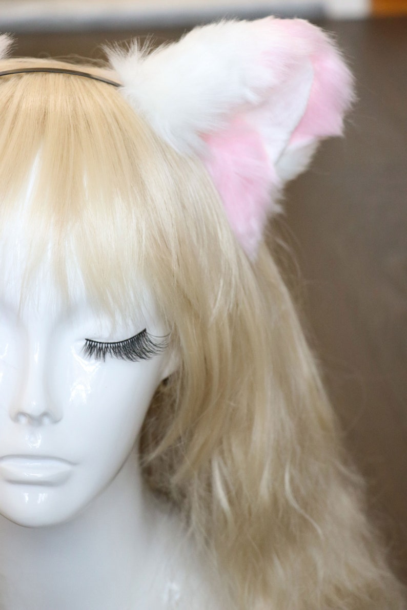 Puede incluir: Una cabeza de maniqu&iacute; blanca con cabello rubio que lleva una diadema de orejas de gato rosa y blanca.