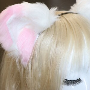 Puede incluir: Diadema de orejas de gato de piel sint&eacute;tica blanca y rosa. La diadema se lleva en una peluca rubia.