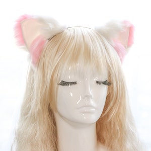 Puede incluir: Una diadema blanca con orejas de gato de pelo rosa. La diadema se lleva en un maniqu&iacute; con el pelo largo y rubio.