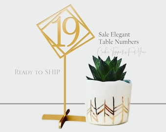 May include: Gold geometric table number card with the number 19 on a gold stand. The card is in the shape of a diamond with a geometric design. The stand has a cross base.  Sale Elegant Table Numbers Cake Toppers For You.