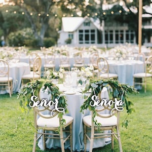 May include: Two chairs decorated with greenery and white signs that say "Se&ntilde;or" and "Se&ntilde;ora" at a wedding reception.