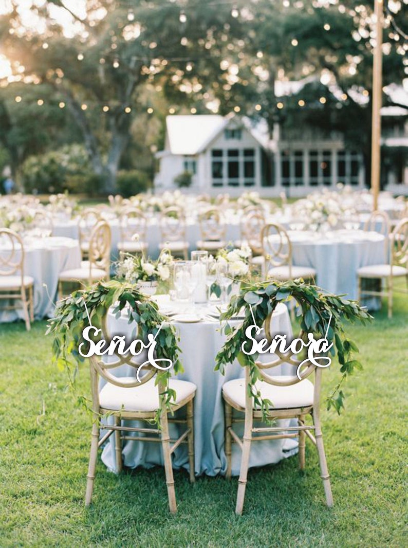 May include: Two chairs decorated with greenery and white signs that say "Se&ntilde;or" and "Se&ntilde;ora" at a wedding reception.