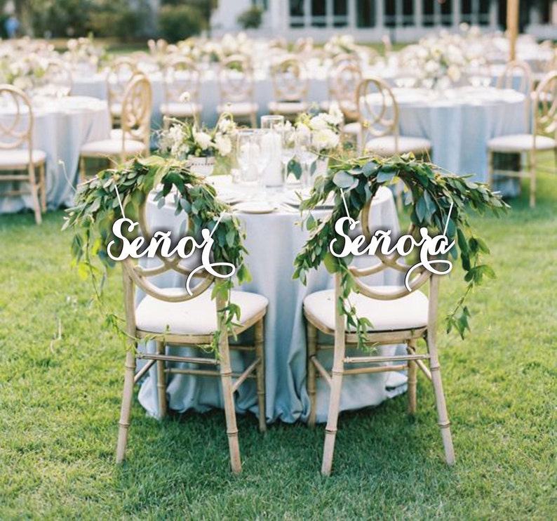 May include: Two wooden chairs with greenery draped over the back. The chairs are decorated with white wooden signs that say "Se&ntilde;or" and "Se&ntilde;ora".