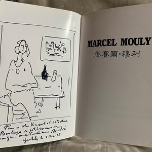May include: A black and white sketch of a person sitting at a table with a bottle and a glass. The text "Pom u Am Vineant at catte chine Chaguri auce foute mon mits Zurhly le 3 dec 98" is written below the sketch. The text "MARCEL MOULY 馬賽爾&middot;穆利" is written in black on a white background.