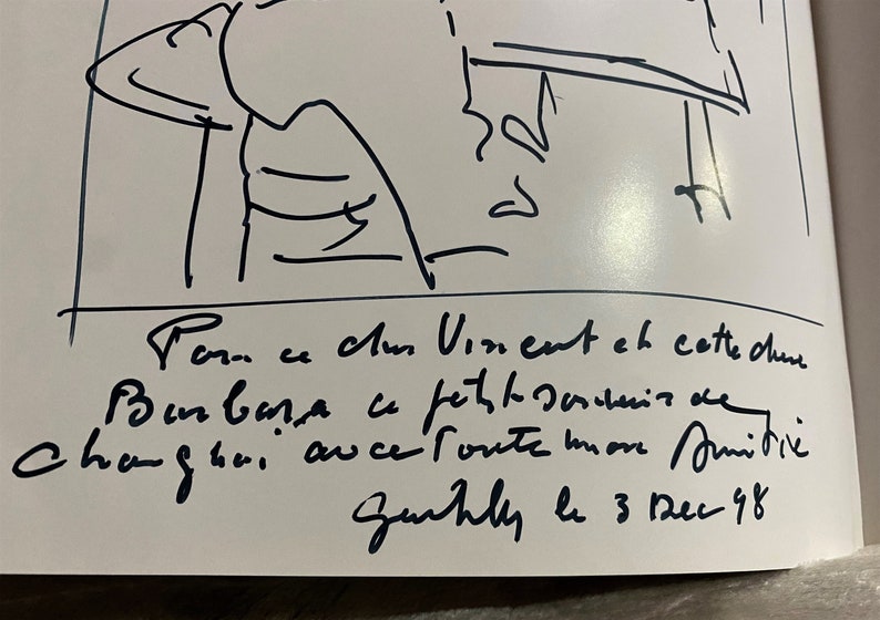 May include: Black and white sketch of a person sitting at a table. The text below the sketch reads "Tom ce chum Vinent en cette dure ce mom Changhai auce route more unitive Zurhly le 3 Dec 98".
