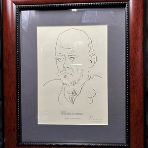 Op de afbeelding: Ingelijste lijntekening portret van een man door Picasso. Het kunstwerk zit in een donkerbruine houten lijst met een zwarte rand. De tekening staat op crèmekleurig papier en bevat de handtekening van de kunstenaar.