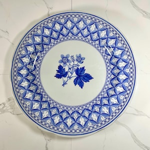 May include: A white ceramic plate with a blue and white floral design. The plate has a scalloped edge and a geometric pattern around the rim.