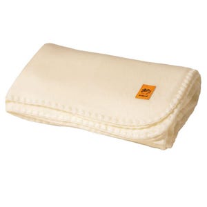 May include: Folded ivory-colored blanket with a stitched edge. An orange label with text is visible on the blanket. The blanket is made of a soft, warm material.