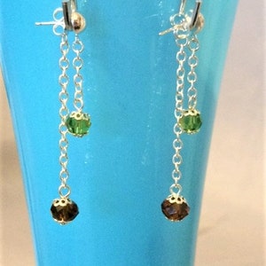 Puede incluir: Un par de pendientes de plata con dos cuentas facetadas verdes y dos marrones. Los pendientes cuelgan de un gancho de plata.