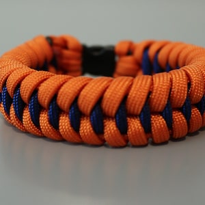 May include: A braided bracelet with orange and navy blue paracord. The bracelet is made with a woven pattern.