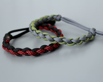 Può includere: Due braccialetti intrecciati in paracord. Uno è nero e rosso, l'altro è verde e grigio.