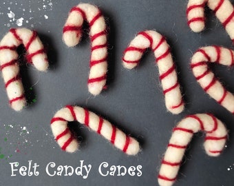 Puede incluir: Una colección de ocho bastones de caramelo de fieltro en rojo y blanco. Los bastones de caramelo están dispuestos sobre un fondo gris con motas blancas.