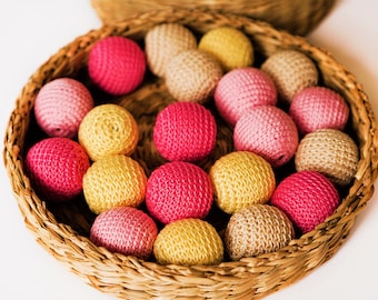 May include: A wicker basket filled with crocheted balls in shades of pink, yellow, and beige. The balls are arranged in a circular pattern and are all the same size.