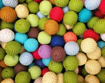 May include: A collection of colourful crocheted balls in various shades of green, blue, red, brown, orange, and cream. The balls are made of yarn and have a textured surface.
