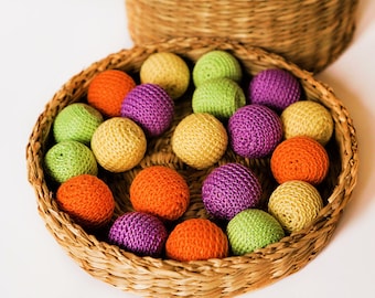 May include: A wicker basket filled with colourful crocheted balls. The balls are in shades of green, orange, purple, and yellow.