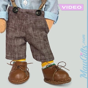 May include: A brown doll wearing a blue and white striped shirt, brown trousers with braces, and brown shoes. The doll is wearing yellow and green socks. The image has the text "VIDEO" and "MauiGifts.com" on it.