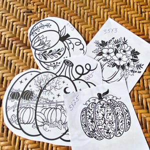 May include: Four black and white pumpkin stencils on white paper. The stencils are different sizes and feature various designs, including a pumpkin with a tree and stars, a pumpkin with a floral design, and a pumpkin with a vine pattern. The stencils are labelled with their dimensions in inches.