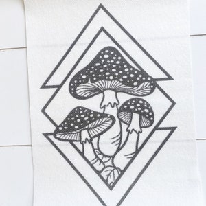 May include: Black and white line drawing of three mushrooms with white spots, inside a geometric diamond shape.