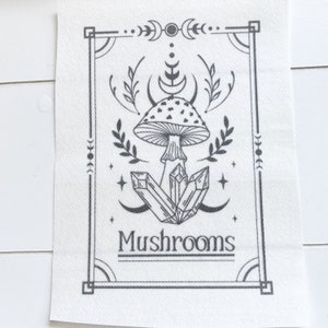 May include: Black and white illustration of a mushroom with crystals and a crescent moon design. The text "Mushrooms" is below the image.