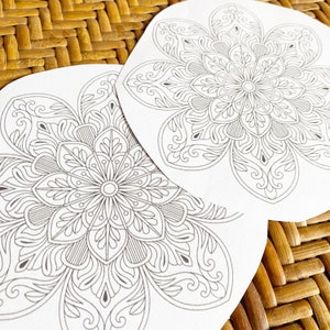 May include: Two white paper circles with intricate black mandala designs. The mandalas are symmetrical and feature floral patterns.