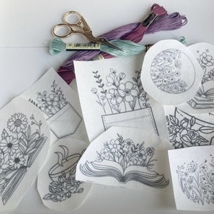 May include: A set of embroidery patterns featuring floral designs, a book, a cup, and a pocket. The patterns are printed on white fabric and are ready to be stitched.