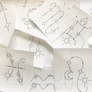 May include: A collection of white cards with black ink drawings of zodiac signs. The signs include Sagittarius, Aquarius, Gemini, Pisces, and Virgo.