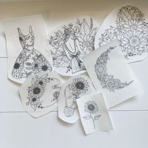 May include: A set of nine black and white iron-on transfers featuring sunflower designs. The designs include a dress, a lightbulb, a crescent moon, a sunflower in a paint palette, and a single sunflower.