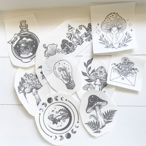 May include: A set of nine black and white iron-on patches featuring various mushroom designs. The patches include mushrooms with eyes, mushrooms in a lightbulb, mushrooms in an envelope, and mushrooms with a crescent moon.
