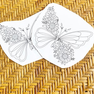 May include: Two black and white printable coloring pages featuring a butterfly with sunflower accents. The butterfly is surrounded by flowers and leaves.