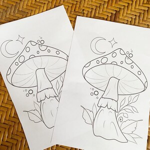 May include: Two black and white colouring pages featuring mushroom illustrations with crescent moons and stars. The mushrooms have white spots and are surrounded by leaves.