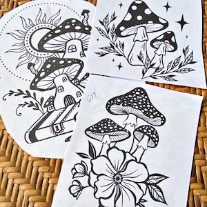 May include: Three black and white illustrations of mushrooms with intricate details. The first illustration features a mushroom with a house inside and a book with a keyhole. The second illustration shows a mushroom with white dots and a leafy branch. The third illustration depicts three mushrooms with a large flower.