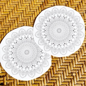 May include: Two white paper mandala colouring pages with intricate designs. The mandalas are circular and feature a variety of geometric patterns.
