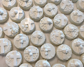Peut inclure: Une assiette de biscuits Oreo recouverts de chocolat blanc décorés de croix blanches et de fleurs blanches. Les biscuits sont disposés en cercle sur une assiette blanche.
