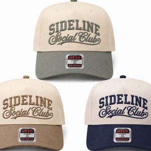 May include: Three baseball caps with cream-colored crowns and contrasting brims in olive green, tan, and navy blue. Each cap features the embroidered text "SIDELINE Social Club" on the front and an Otto Classic Fit sticker on the brim.