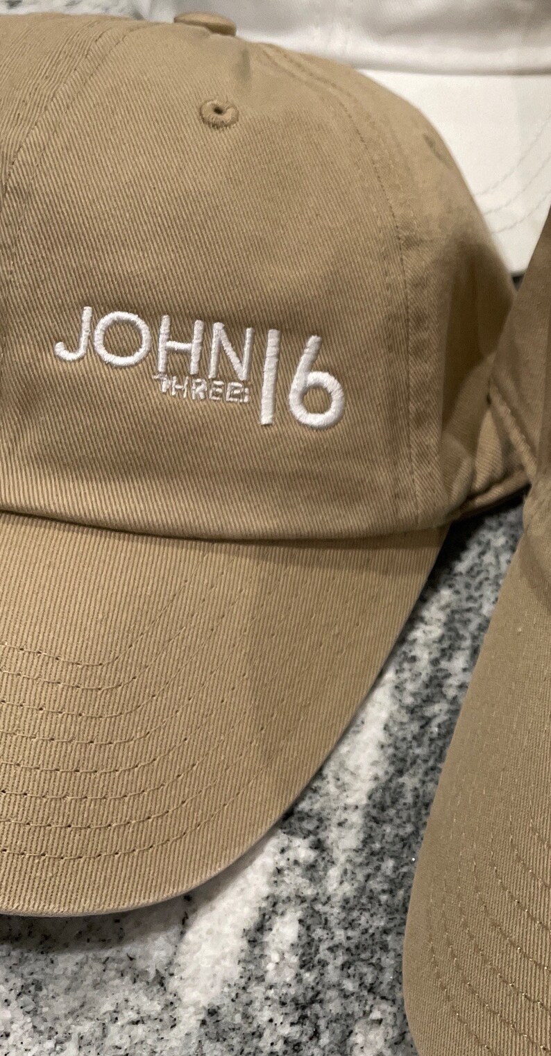 May include: A tan baseball cap with white embroidered text that reads "JOHN 16 THREE".