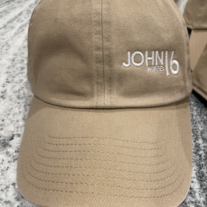 May include: A tan baseball cap with a white embroidered logo that says "JOHN16 THREE".