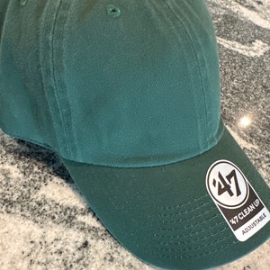 May include: A dark green baseball cap with a black and white '47 Clean Up Adjustable' logo on the side.