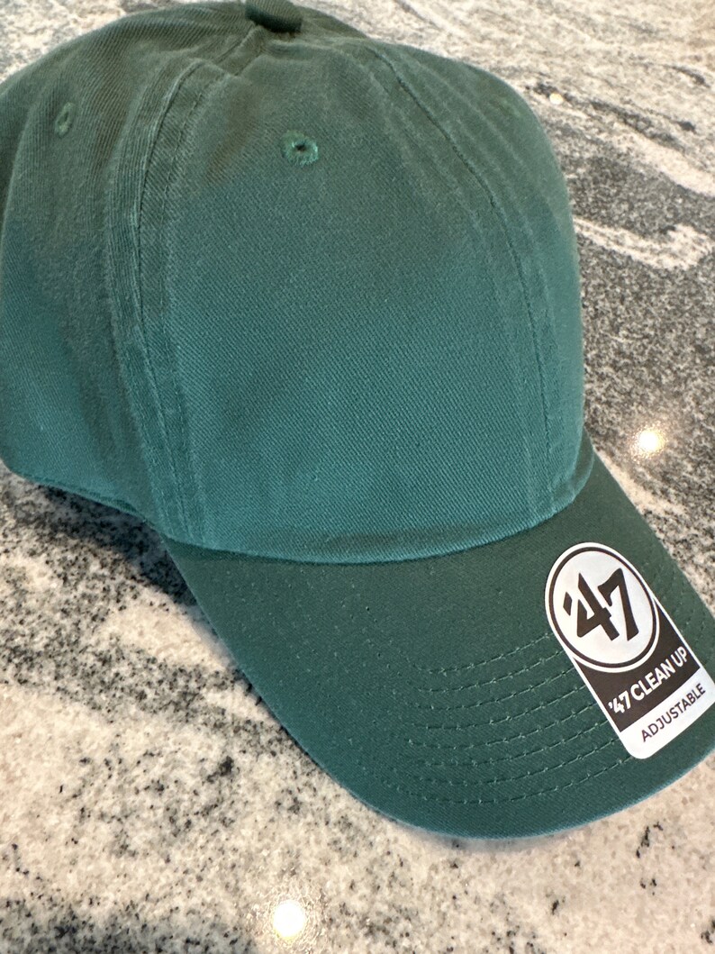 May include: A dark green baseball cap with a black and white '47 Clean Up Adjustable' logo on the side.