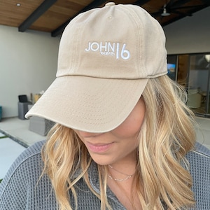 May include: A tan baseball cap with white embroidered text that reads "JOHN 16 THREE".