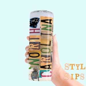 May include: A cylindrical tumbler featuring the Carolina Panthers logo and the words "NORTH CAROLINA" in a collage of various fonts and colors. A squirrel image is also present. The tumbler is held against a light blue background.
