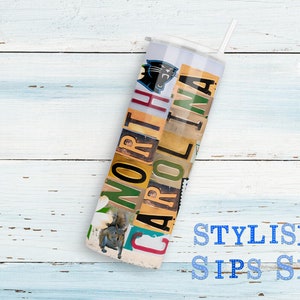 May include: A white tumbler with a straw, featuring the text "NORTH CAROLINA" in a collage of license plate letters. The design includes a Carolina Panthers logo and a squirrel image. The words "STYLISH SIPS SK" are also visible.