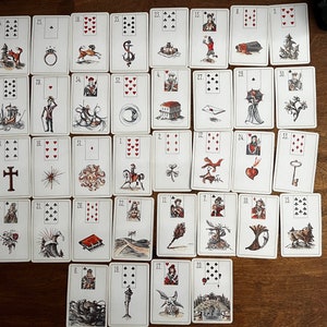 May include: A collection of tarot cards laid out on a wooden surface. Each card features a unique black and white illustration with a number and suit symbol. The cards depict various scenes and symbols, such as a ring, a cross, and a key.