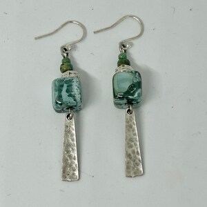 May include: A pair of silver dangle earrings with green and white square-shaped beads and hammered silver accents.