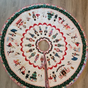 May include: A circular Christmas tree skirt featuring a white center with a repeating pattern of nutcracker figures and red scalloped borders. The outer edge is a wide green band with a festive print, finished with a red and white striped trim.