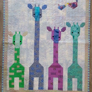 Puede incluir: Un tapiz de pared acolchado con cuatro diseños de jirafas coloridas con un pequeño pájaro en la esquina superior derecha. Las jirafas están hechas de tela de patchwork en tonos de azul, verde, morado y rosa.