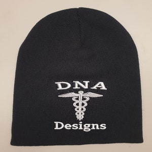 Peut inclure: Bonnet noir en tricot avec un symbole médical brodé en blanc et le texte "DNA Designs".