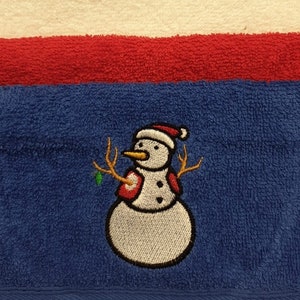 Può includere: Una collezione di asciugamani colorati. Gli asciugamani sono in vari colori, tra cui nero, marrone, giallo, lavanda, rosa, grigio, bianco, rosso e blu. Un asciugamano blu presenta un pupazzo di neve ricamato.