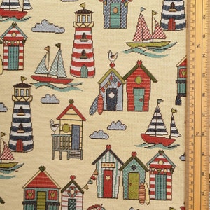 May include: A fabric with a repeating pattern of beach huts, sailboats, lighthouses, and clouds. The huts have red, blue, and green doors and roofs. The sailboats have red hulls and striped sails. The lighthouses are red and white or blue and white.
