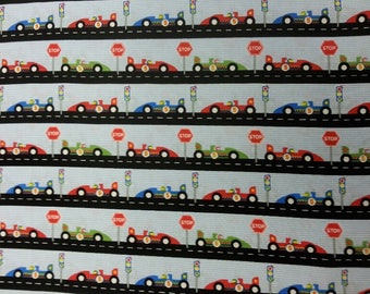 May include: A repeating pattern of race cars in red, green, and blue, each with the number 5, driving on black roads with stop signs and traffic lights. The background is a light blue with vertical stripes.