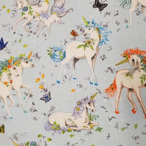 May include: Light blue fabric featuring white unicorns with colorful manes and golden horns. The unicorns are adorned with floral accents and surrounded by butterflies and leaves. The fabric has a whimsical, fantasy theme.